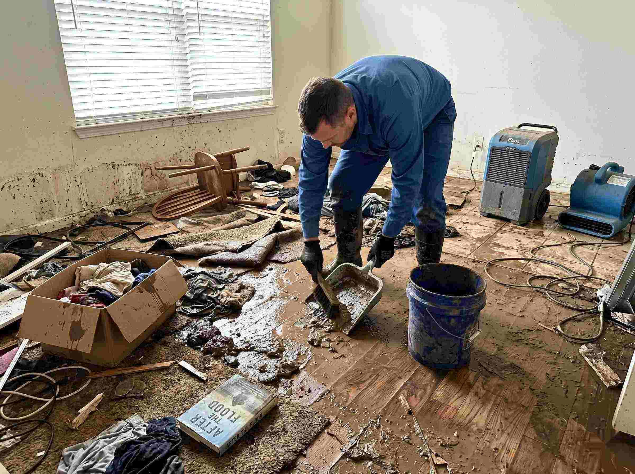 Professional realistic photo of a technician performing mud and debris removal after a home flood in Yuma, showing soaked furniture, wet flooring, and scattered debris during post-flood cleanup.